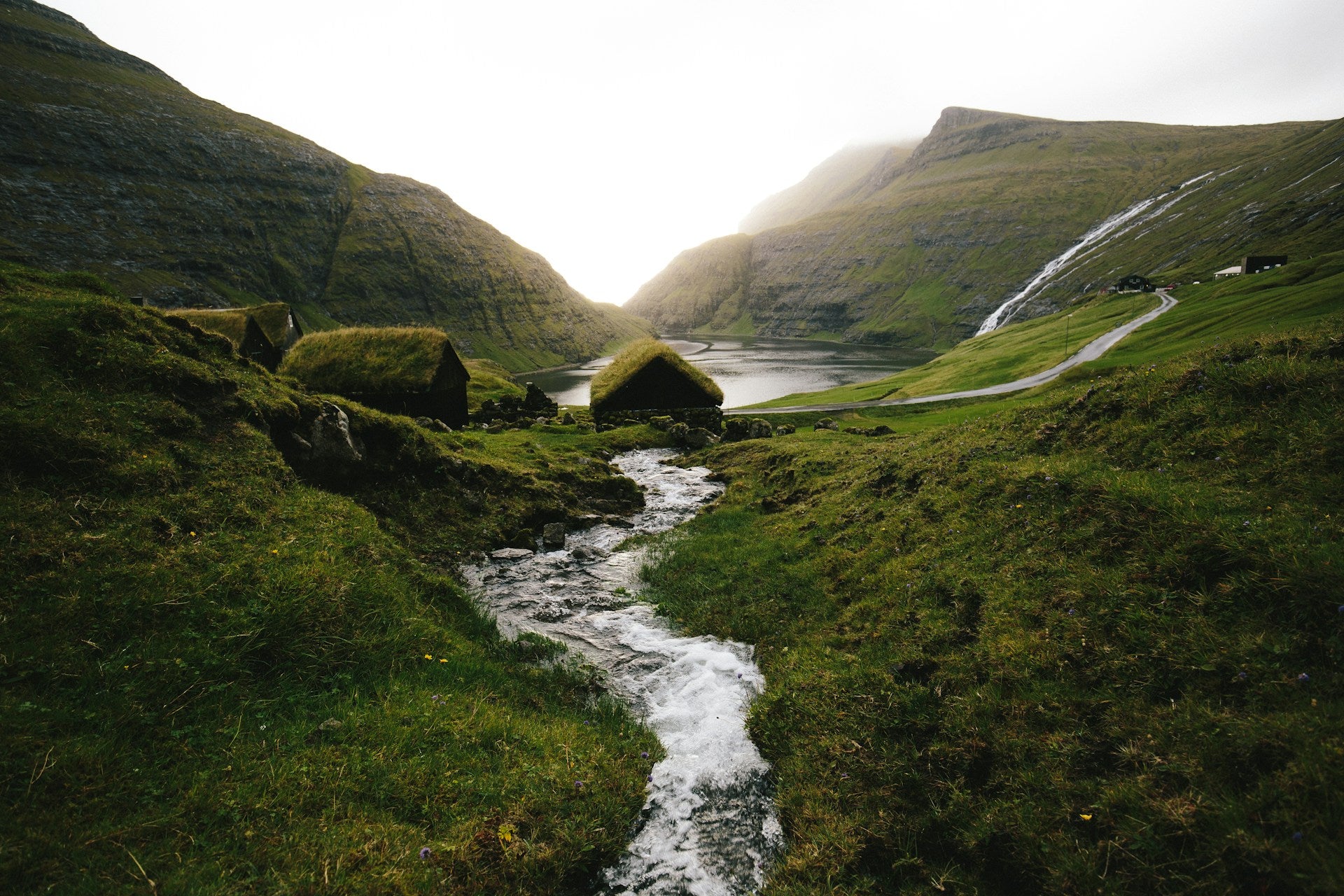 Small, moss-covered houses near a river in between green hills